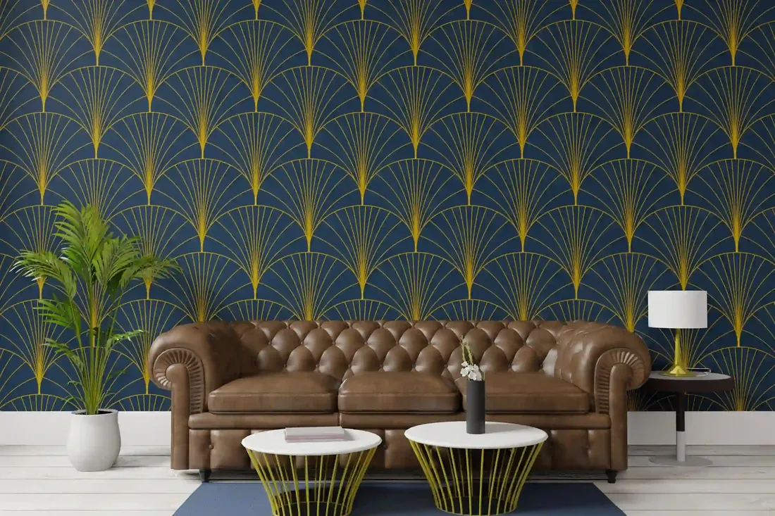 Navy wallpaper with a gold art deco fan pattern behind a brown leather chesterfield sofa