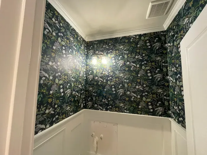 Small room with dark botanical wallpaper above white wainscoting