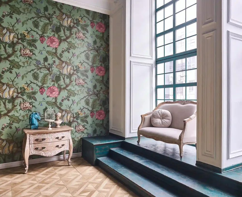 Green floral wallpaper with pink roses beside a tall window and a vintage loveseat